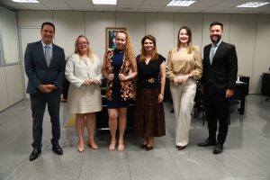 Um grupo de seis pessoas, três homens de terno e três mulheres com diferentes trajes de negócios e casuais elegantes, posando em um escritório.