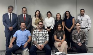 Um grupo de dez pessoas, cinco homens e cinco mulheres, vestindo trajes de negócios e casuais, posando em um escritório, com uma mesa coberta com pratos e copos em primeiro plano.