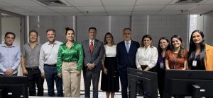 Um grupo de onze pessoas, homens e mulheres, vestindo trajes de negócios e casuais, posando lado a lado em um escritório, com monitores de computador na frente.