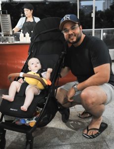 Imagem de um homem agachado com um bebê no carrinho.