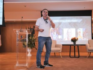 Homem branco, usando camiseta branca e calça jeans clara.