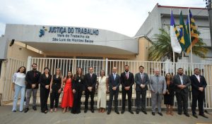 Foto de 15 pessoas em frente ao prédio da Vara do Trabalho de São Luís de Montes Belos. São sete mulheres e oito homens. Eles usam roupas formais e estão de pé, lado a lado, sorrindo e posando para foto.