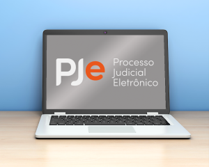 Imagem de um notebook com a tela aberta e sobre uma superfície amadeirada. Na tela do equipamento aparece a logomarca do PJe e o texto Processo Judicial Eletrônico