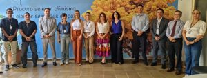 Um grupo de 13 pessoas (seis homens e sete mulheres) está de pé em um corredor, posando para a foto. A parede de fundo tem a imagem de um ipê amarelo e uma citação.