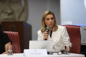 Mulher vestindo terno branco fala ao microfone