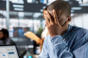 Homem negro no ambiente de trabalho com as mãos no rosto, aparentemente chateado