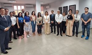 Um grupo de aproximadamente quinze pessoas, homens e mulheres em trajes de negócios e casuais, posando em pé em um escritório