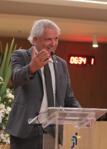 Homem de pele clara e cabelos grisalhos falando ao microfone.