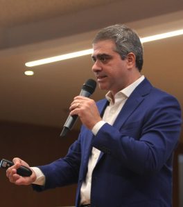 Homem de pele clara e cabelos grisalhos falando ao microfone