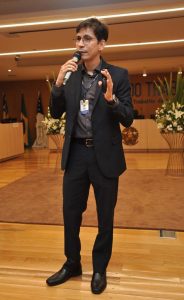 Homem de pele clara e cabelos castanhos falando ao microfone