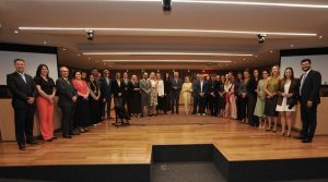 Pessoas reunidas no palco de um auditório. Elas usam roupas formais e estão sorrindo e posando para a foto.