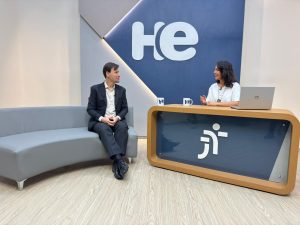 Um homem sentado em uma poltrona e uma mulher numa bancada. Eles olham para a câmara. Ao fundo, a logomarca do programa hora extra. Embaixo da bancada, a logomarca da Justiça do Trabalho