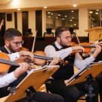 Músicos sentados tocando violino e flauta